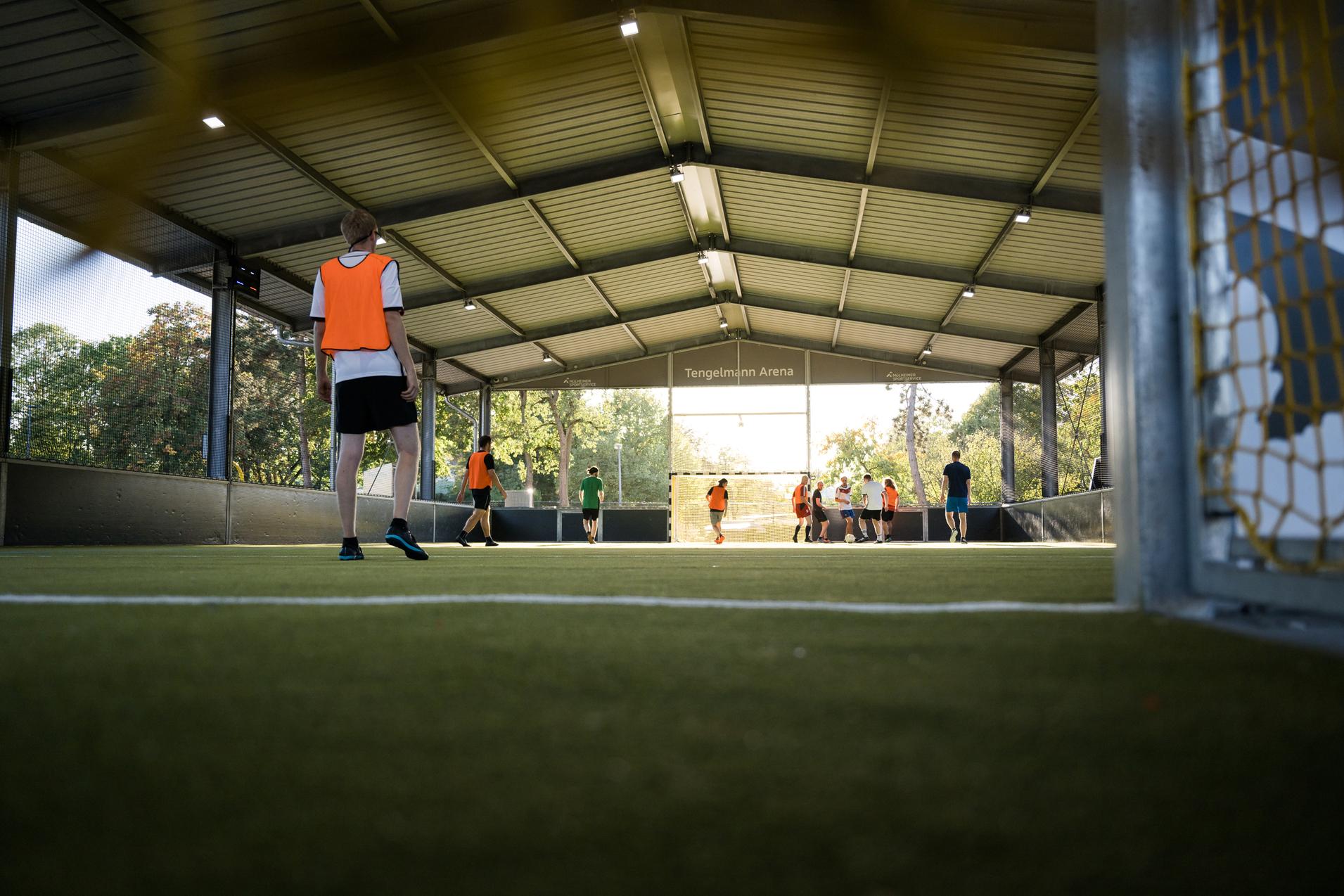 Gruppe von Jugendlichen in orangefarbener Spielformation auf einem Soccerfeld in der Tengelmann Arena.